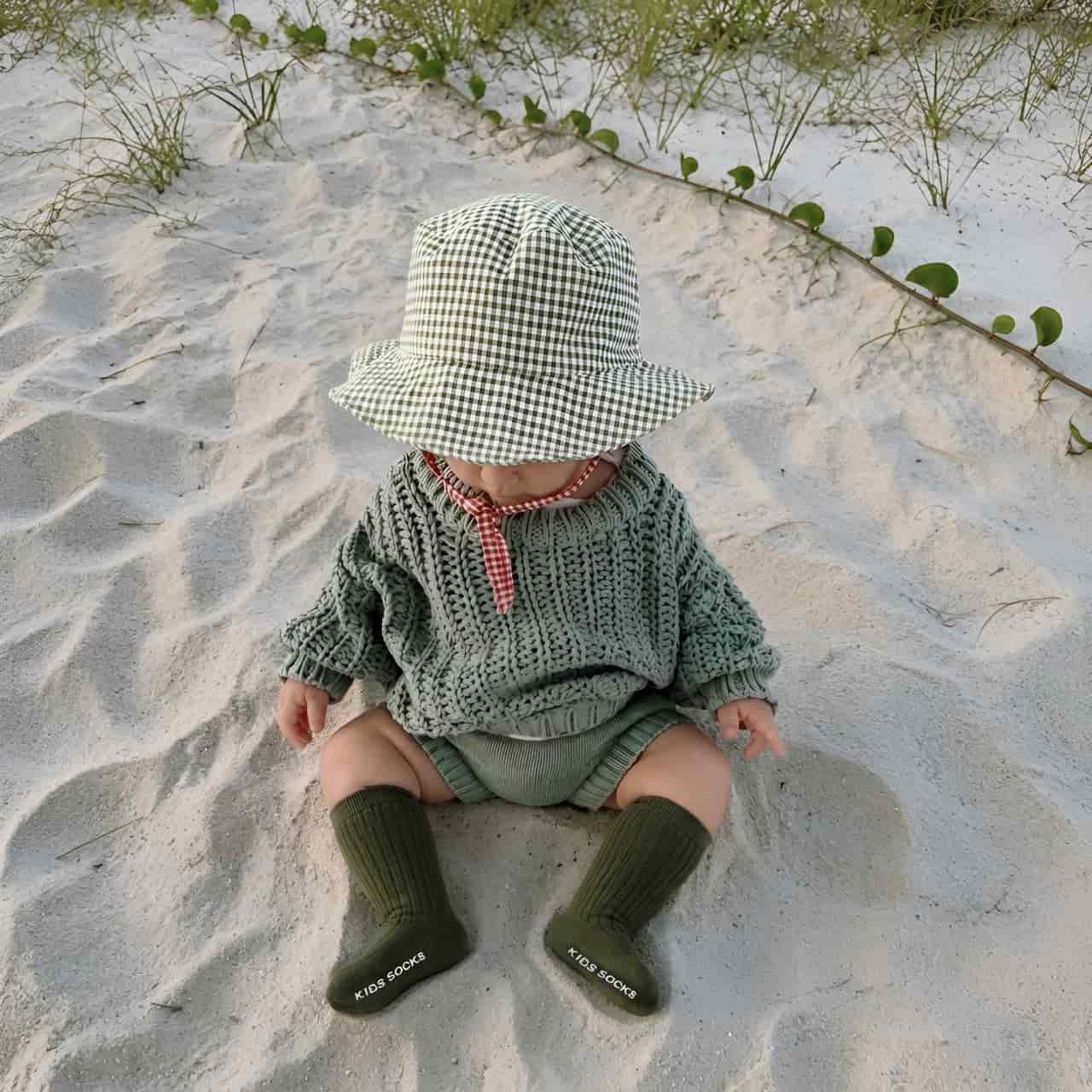 Baby wearing olive green ribbed knee-high socks with knitted outfit on the beach