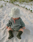 Baby wearing olive green ribbed knee-high socks with knitted outfit on the beach