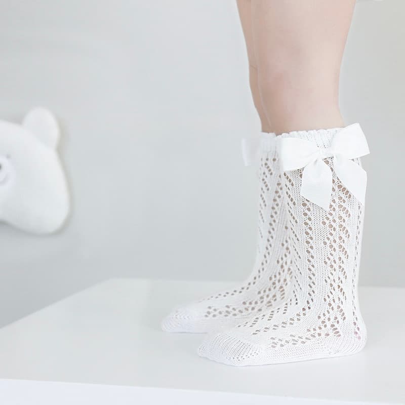 White baby lace knee-high socks with bow, breathable cotton knit worn by infant girl
