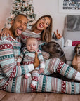 Family wearing matching Christmas pajamas with baby and dogs in front of Christmas tree