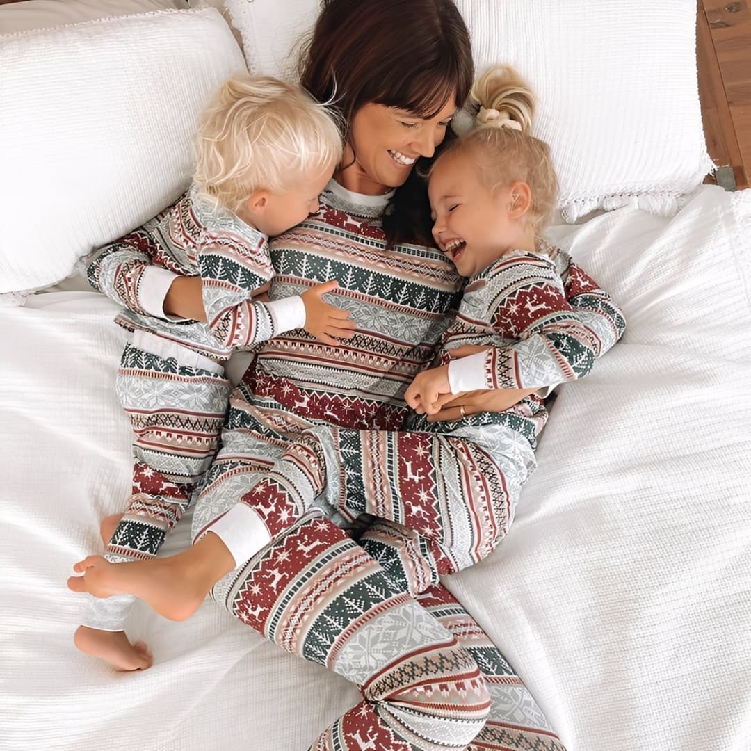 Mother and children in matching holiday pajamas laughing together on bed
