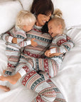 Mother and children in matching holiday pajamas laughing together on bed