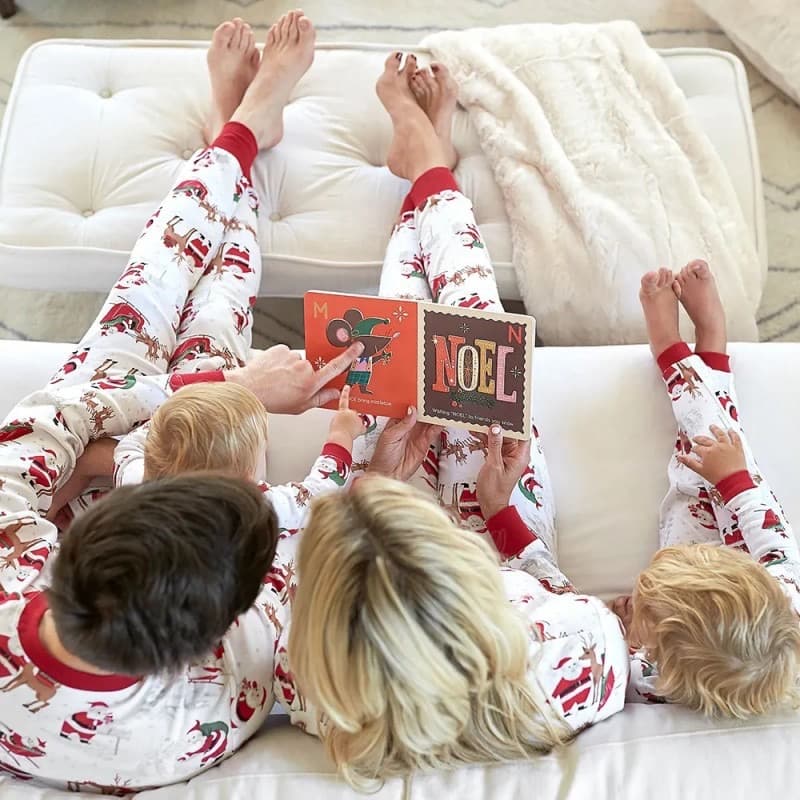 Family in matching Christmas pajamas reading holiday books on couch, cozy festive atmosphere.