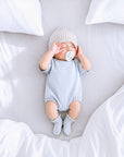Newborn baby wearing grey CloudSoft cotton baby romper with ribbed scallop edge baby socks in soft minimalist neutral nursery setting