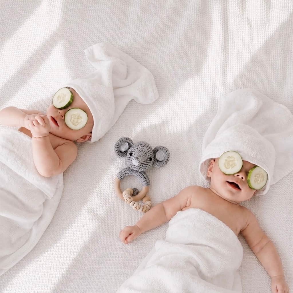 Twin newborn babies relaxing beside a crochet elephant teether with a wooden teething ring and personalised beads, a thoughtful baby shower gift and newborn essential in the UK.