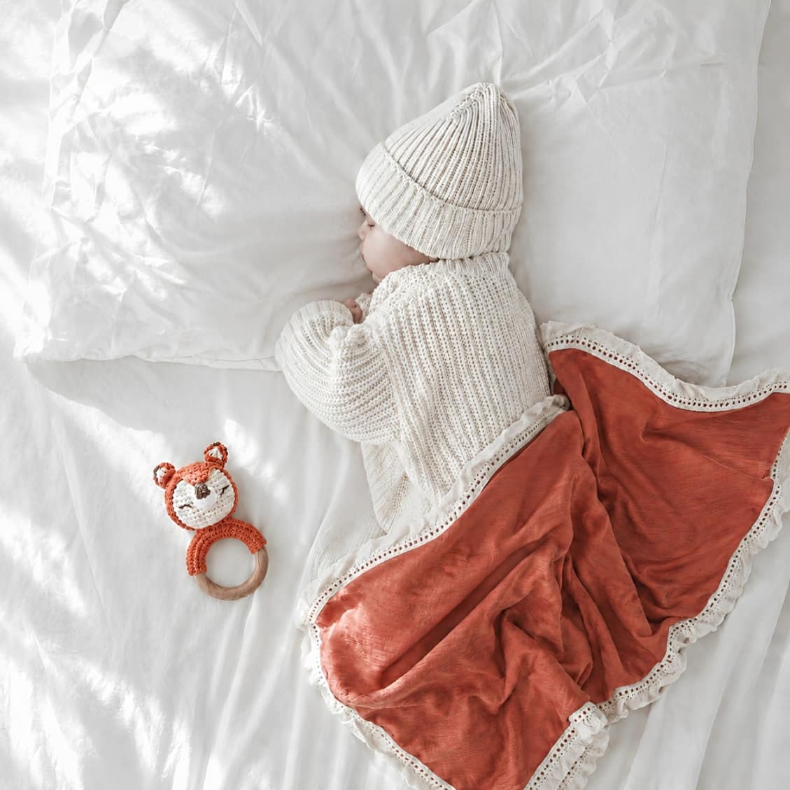 Sleeping newborn baby with crochet fox rattle and coral tassel baby blanket, sensory toy and nursery essential for baby shower gifts.