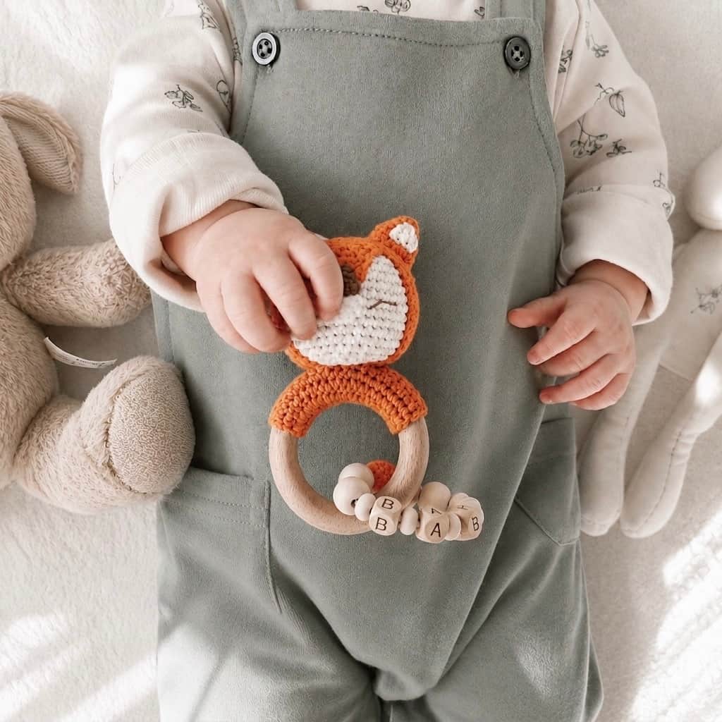 Baby holding a crochet fox teether with a wooden teething ring and personalised wooden beads, a thoughtful newborn gift and baby shower gift in the UK.