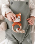 Baby holding a crochet fox teether with a wooden teething ring and personalised wooden beads, a thoughtful newborn gift and baby shower gift in the UK.