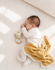 Sleeping newborn baby with a handcrafted crochet lion rattle and soft mustard baby blanket, perfect for sensory play, nursery essentials and baby shower gifts.