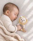 Sleeping newborn baby holding a crochet lion teether with a wooden teething ring, a thoughtful baby shower gift and newborn essential in the UK.