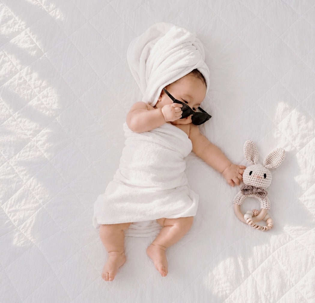 Baby wrapped in a soft white towel beside a crochet rabbit teether with a wooden teething ring, a thoughtful baby shower gift and newborn essential in the UK.