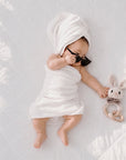 Baby wrapped in a soft white towel beside a crochet rabbit teether with a wooden teething ring, a thoughtful baby shower gift and newborn essential in the UK.