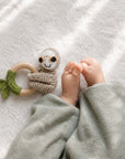 Crochet sloth rattle and wooden baby teether beside a newborn baby, a thoughtful baby shower gift and newborn essential in the UK.