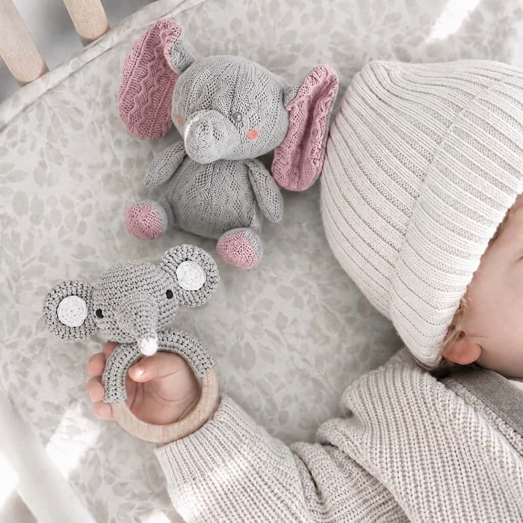 Newborn baby holding a handcrafted crochet elephant rattle beside a matching big-ear elephant comfort toy, a thoughtful baby shower gift and nursery essential.