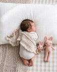 Newborn baby sleeping beside a handcrafted crochet pink bunny comfort toy and matching bunny rattle, a thoughtful baby shower gift and nursery essential for sensory play.