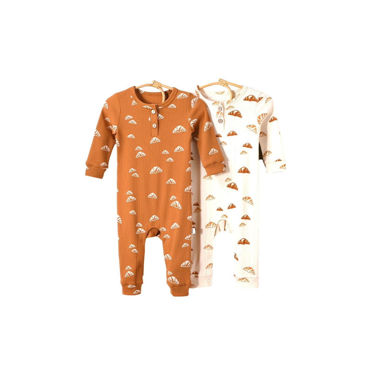 Two cotton baby rompers with croissant print in apricot and cream colors, long sleeves, soft ribbed texture, ideal for boys and girls.