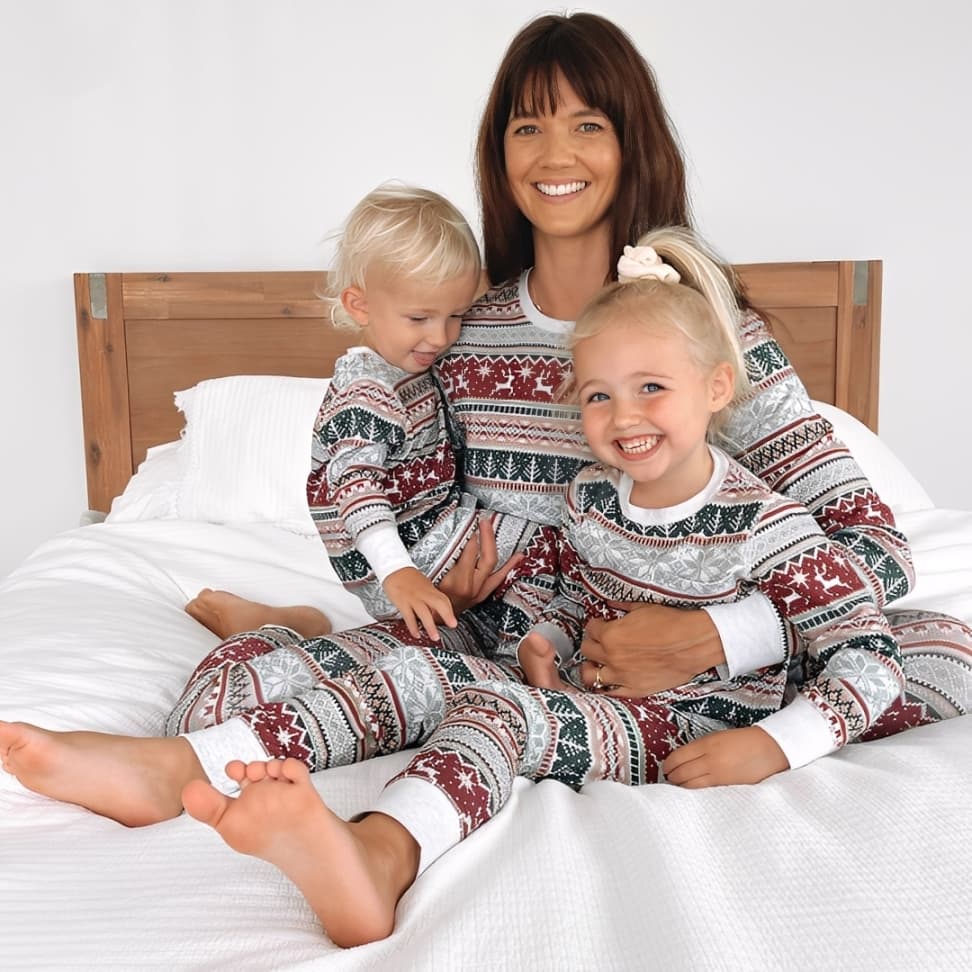 Mom and two children in matching holiday pajamas smiling together on bed