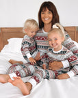 Mom and two children in matching holiday pajamas smiling together on bed