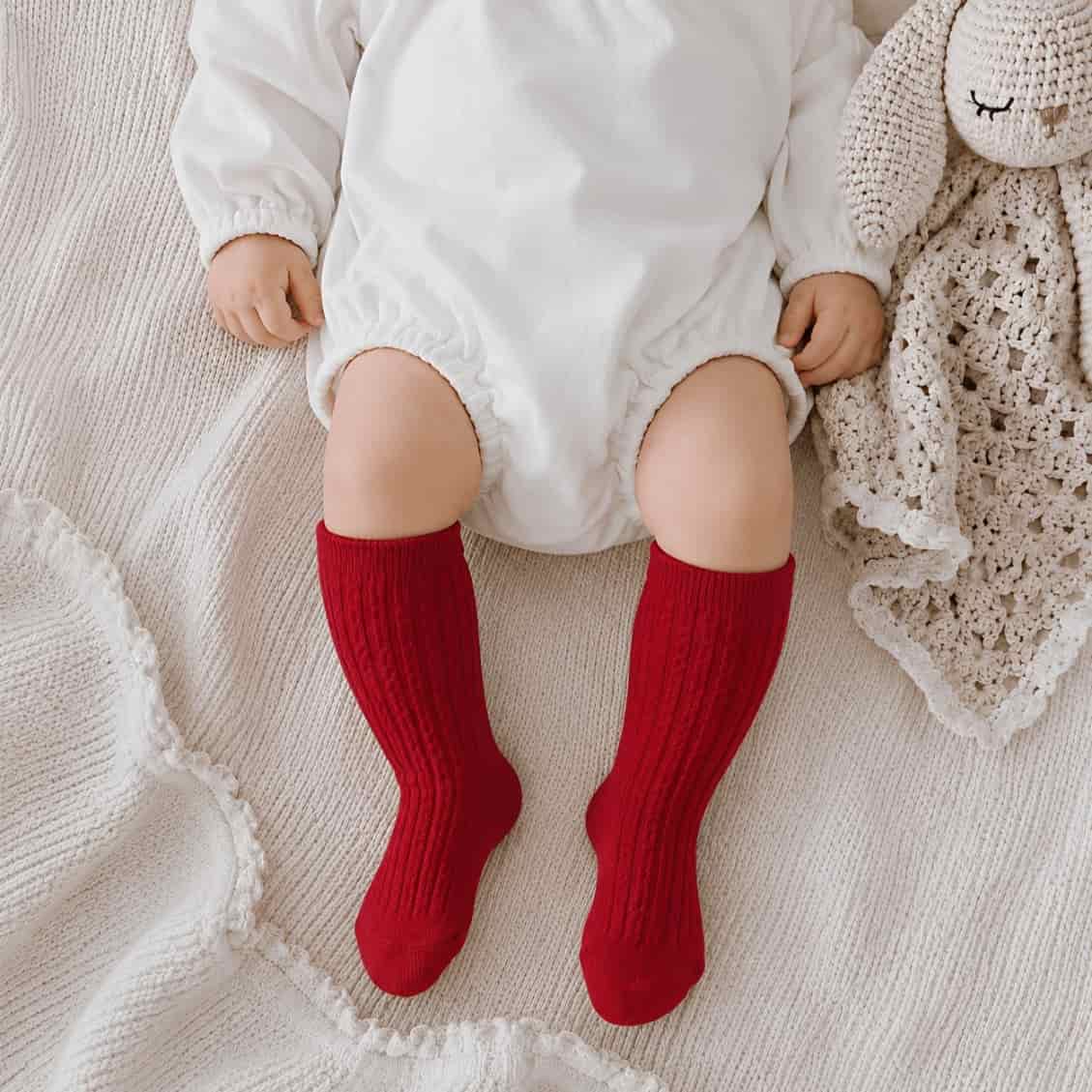 Baby wearing red fluffy fleece knit knee-high socks on soft neutral blanket
