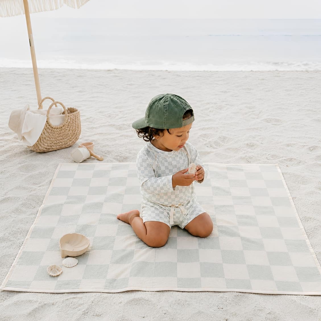 child wearing checkered long sleeve rash guard swim set sitting on beach mat summer outfit