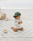 child wearing checkered long sleeve rash guard swim set sitting on beach mat summer outfit