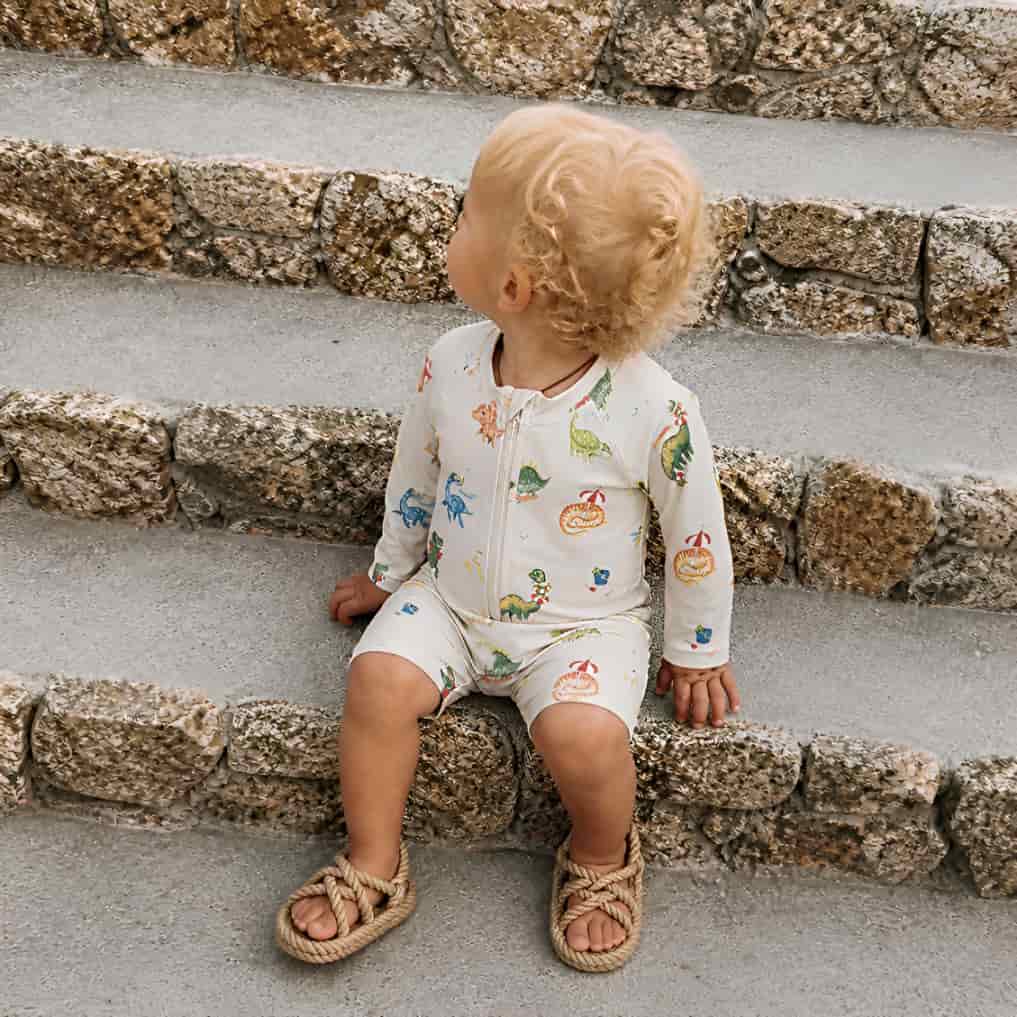 toddler wearing dinosaur print rash guard swimsuit sitting on stone steps UV protection swimwear
