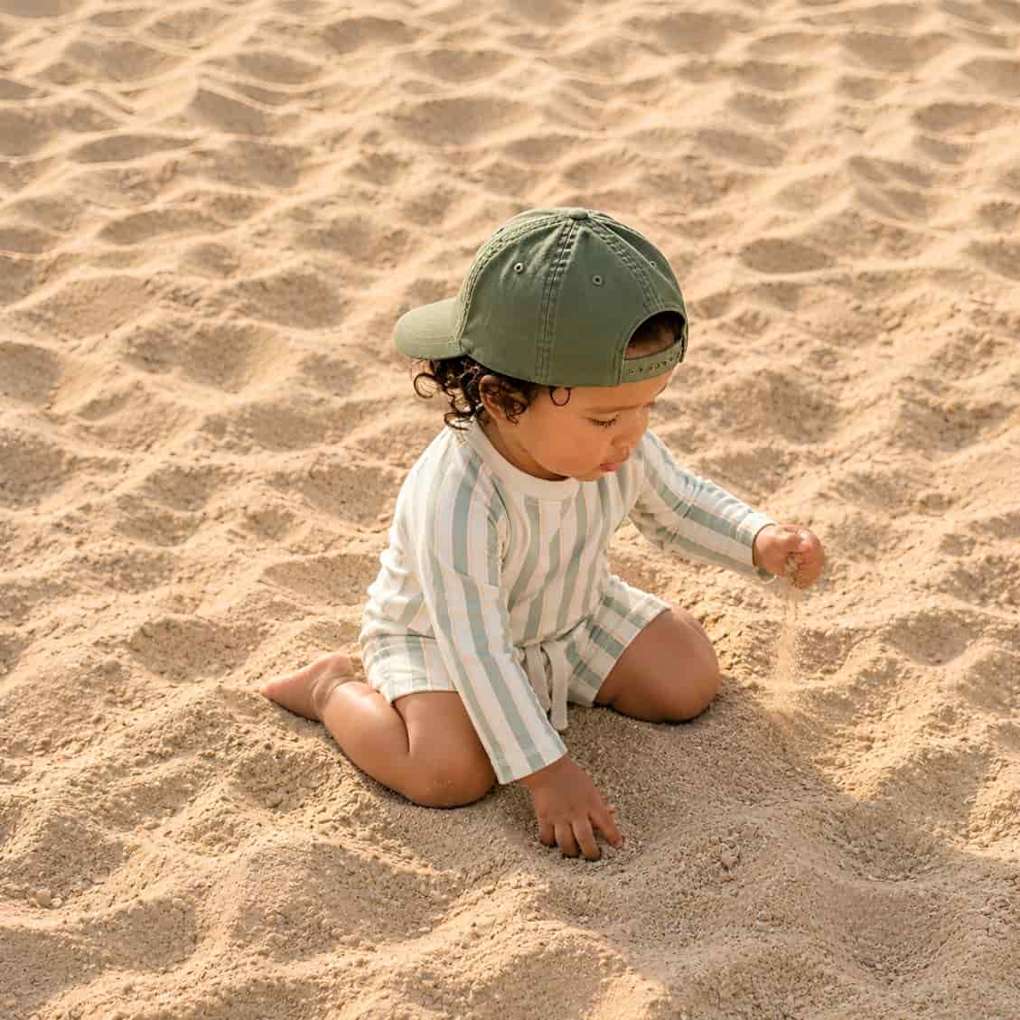 toddler wearing green striped rash guard swim set playing on sandy beach UV protection swimwear