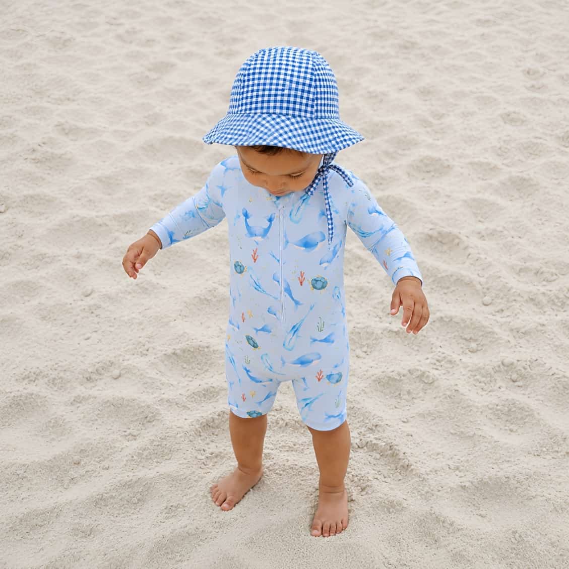 toddler wearing blue ocean whale rash guard swimsuit standing on sand beach UV swimwear
