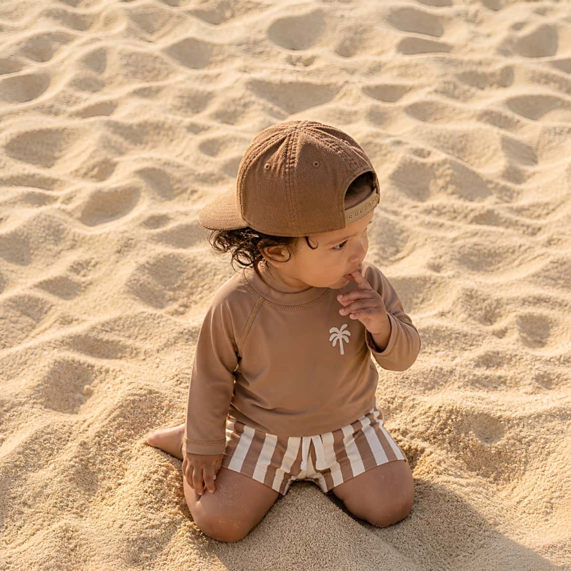 toddler wearing sand stripe palm rash guard swim set sitting on beach sand UV protection swimwear