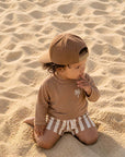 toddler wearing sand stripe palm rash guard swim set sitting on beach sand UV protection swimwear