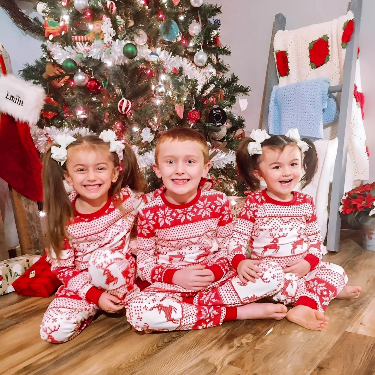 Children wearing red reindeer Christmas matching pajamas by the tree, cozy holiday loungewear
