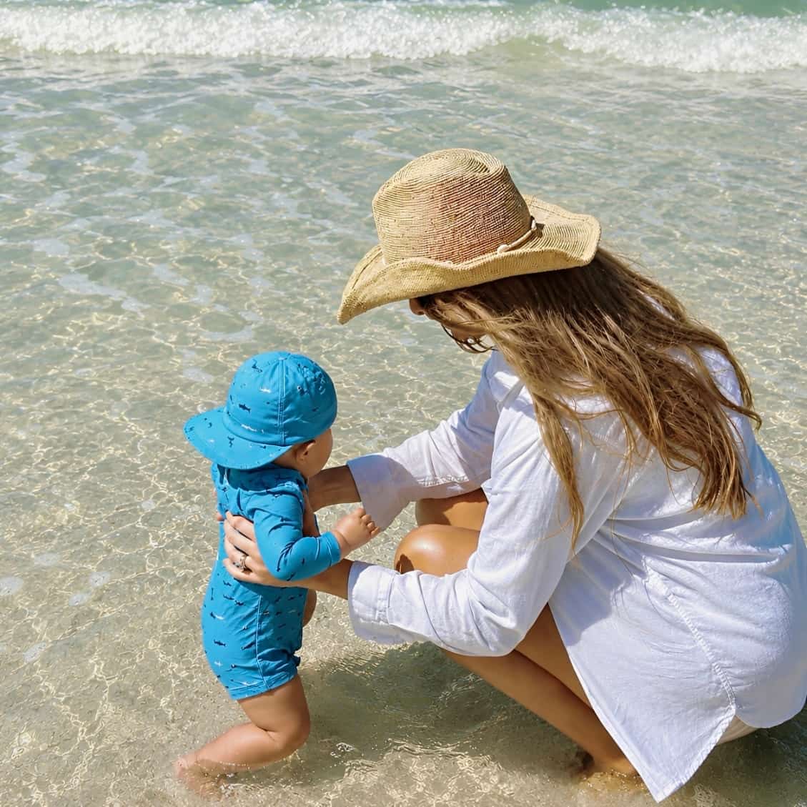 toddler wearing blue shark print rash guard swimsuit standing on sand back view UV swimwear