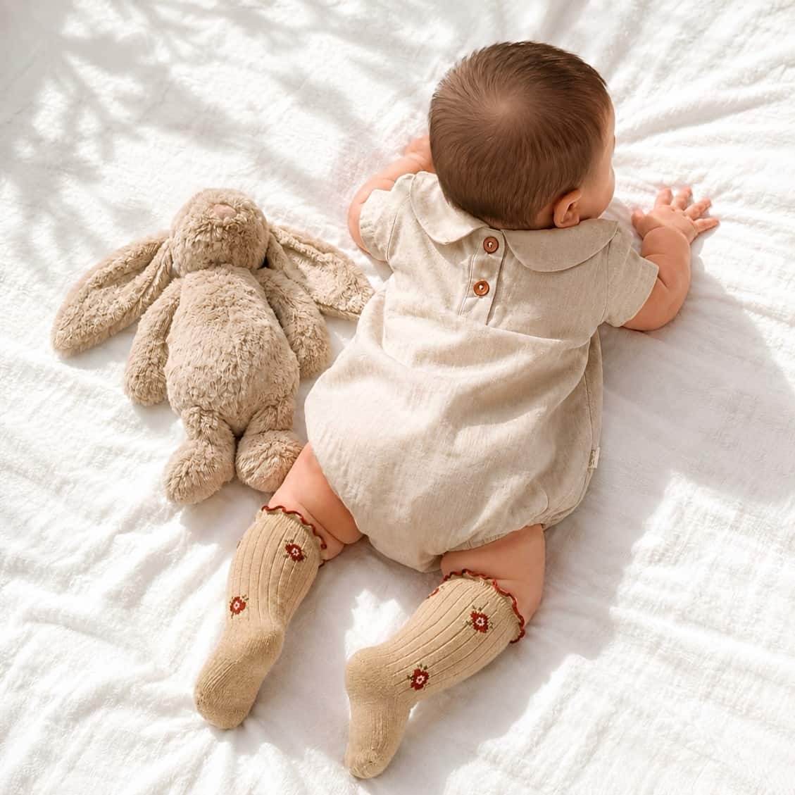Baby wearing neutral linen romper with floral ruffle knit socks in khaki
