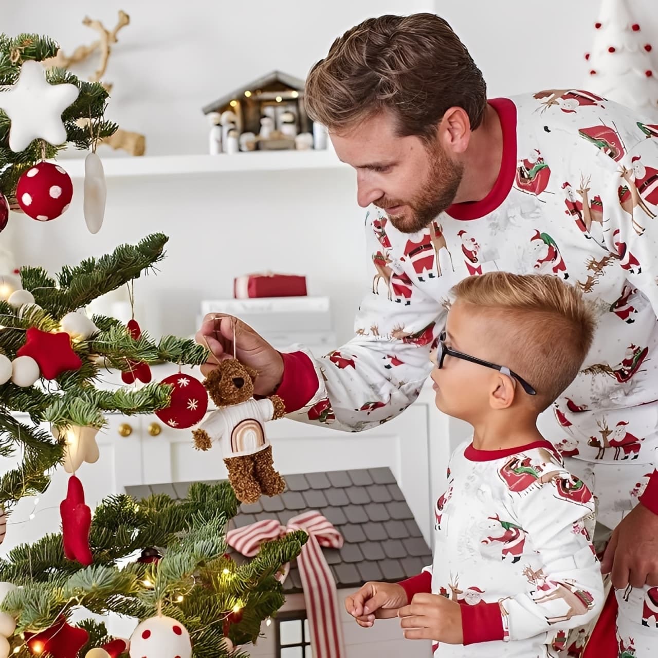 Dad and son in matching Santa print Christmas pajamas decorating Christmas tree together.
