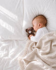 Sleeping newborn baby cuddling a crochet teddy bear rattle with a soft khaki tassel baby blanket, perfect for sensory development and baby shower gifts.