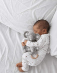 Newborn baby cuddling a crochet elephant toy and wooden elephant rattle set on a soft white nursery bed.