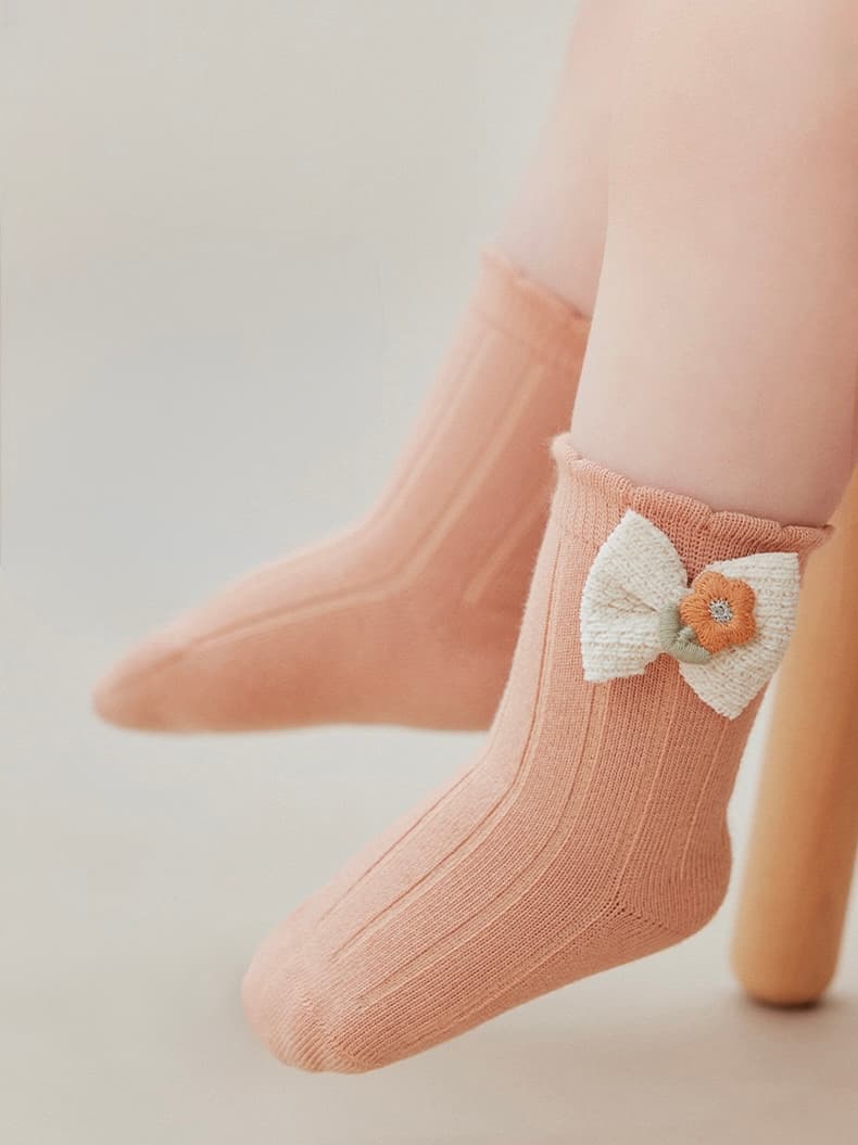Peach cotton baby socks featuring a cute knitted bow and soft ribbed design.
