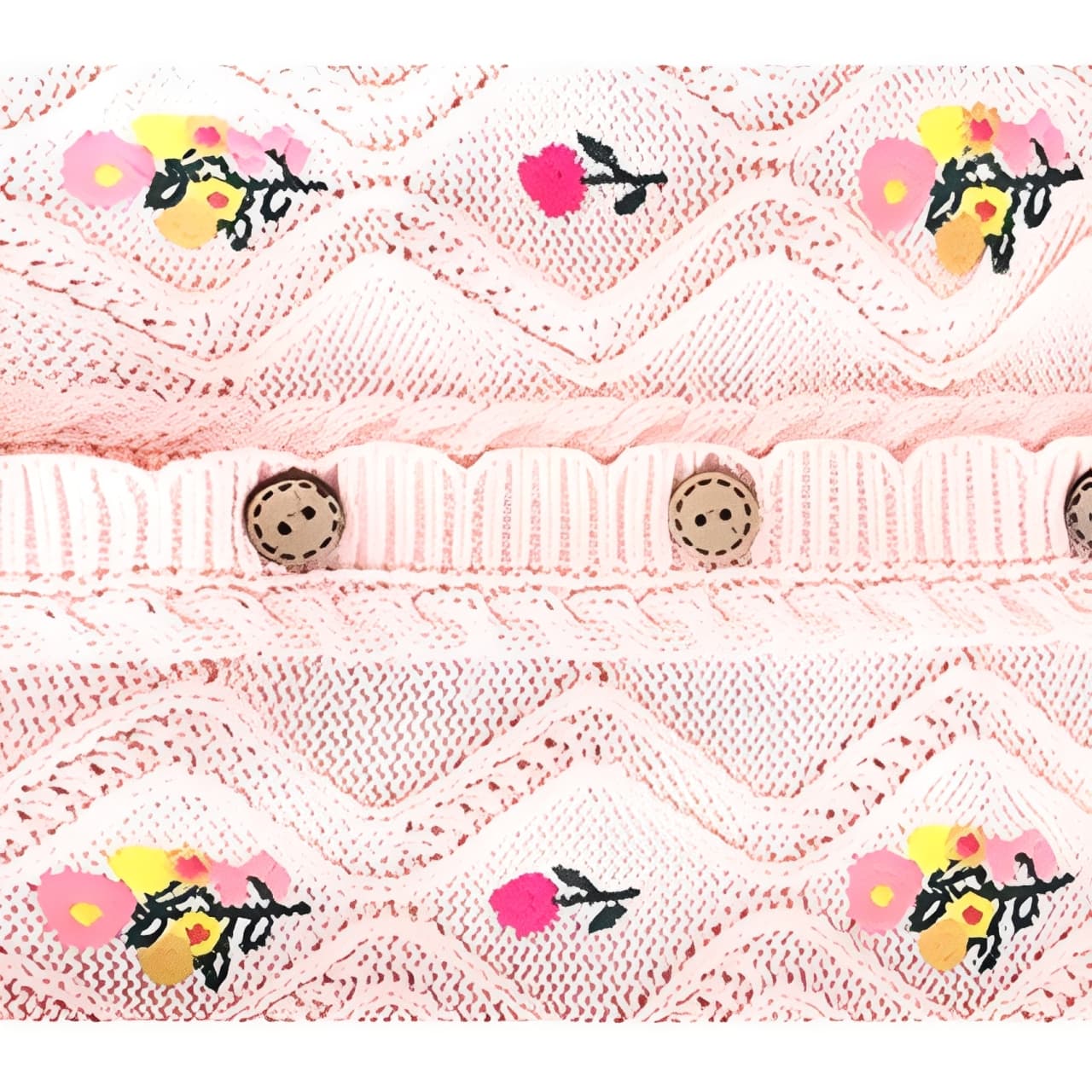 Detailed close-up of floral embroidery and buttons on pink cotton knit baby romper.
