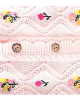 Detailed close-up of floral embroidery and buttons on pink cotton knit baby romper.
