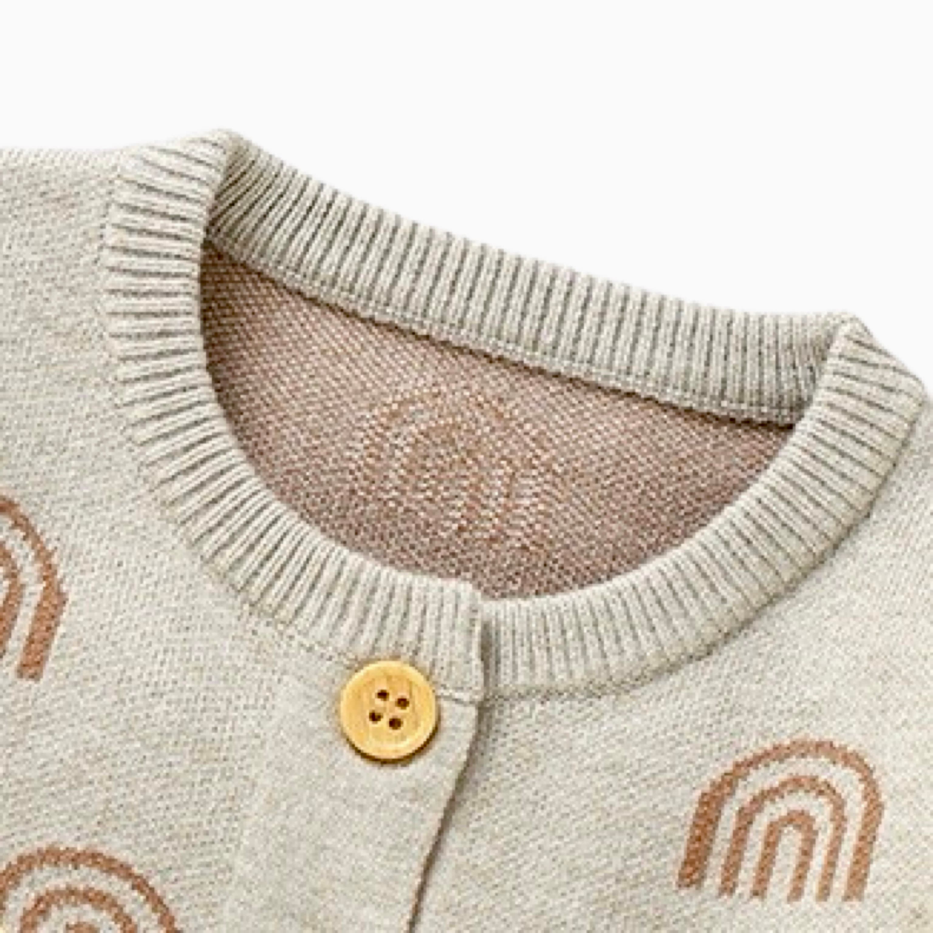Close-up detail of collar and button on rainbow knit baby romper showing fine stitching and soft knitted fabric.
