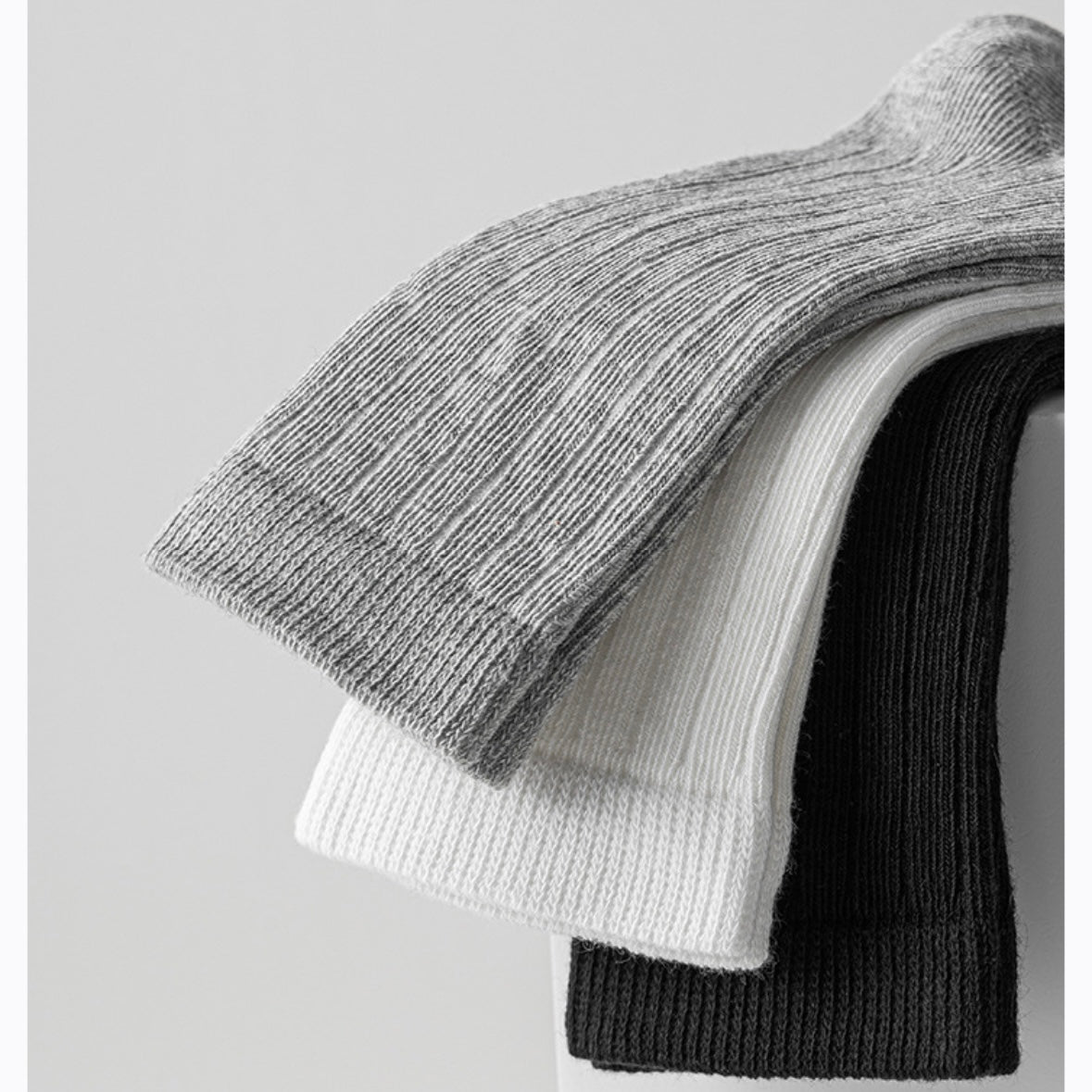 Stack of folded knit sweaters in gray, white, and black on a light gray background