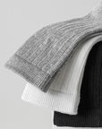 Stack of folded knit sweaters in gray, white, and black on a light gray background
