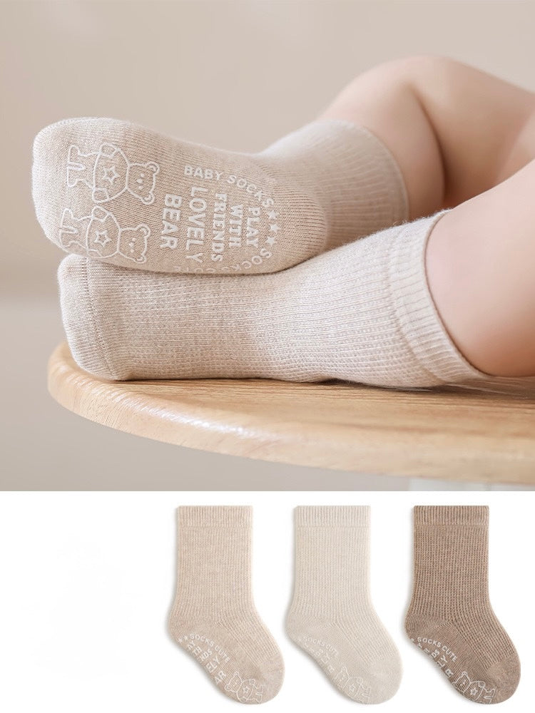 Beige socks with text worn by a child on a wooden stool, with additional pairs displayed below.