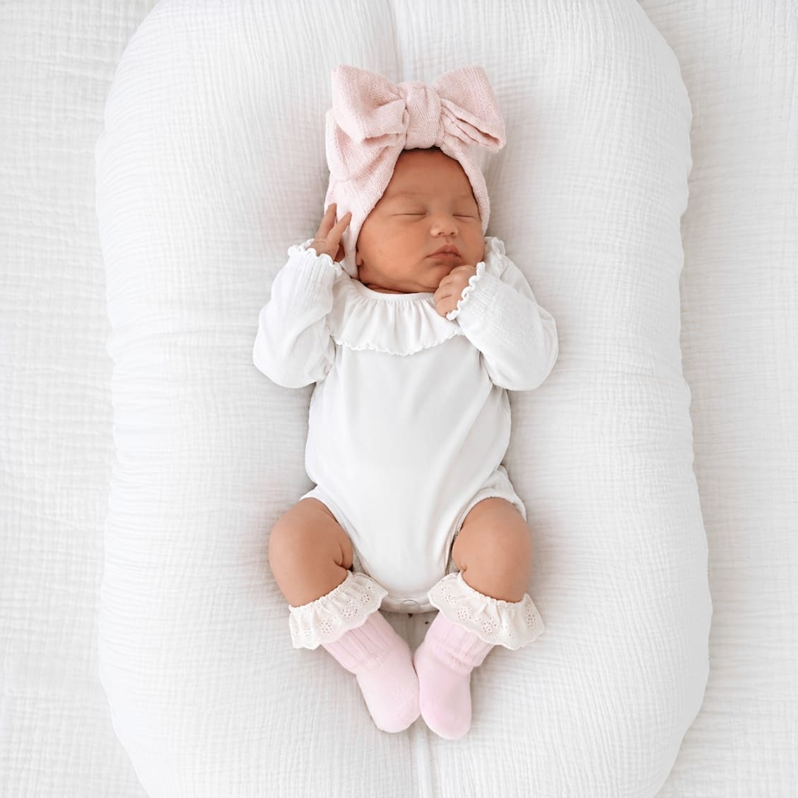 Newborn baby girl wearing a white ruffle collar baby bodysuit with eyelet lace cotton baby socks in soft minimalist nursery setting