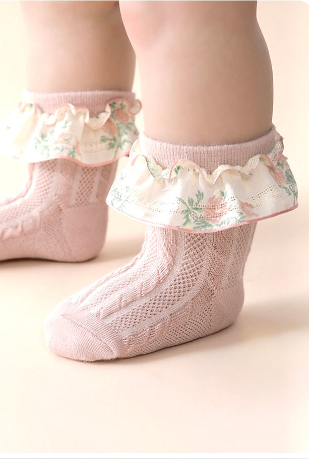 Pink baby socks with floral ruffles on a light background 