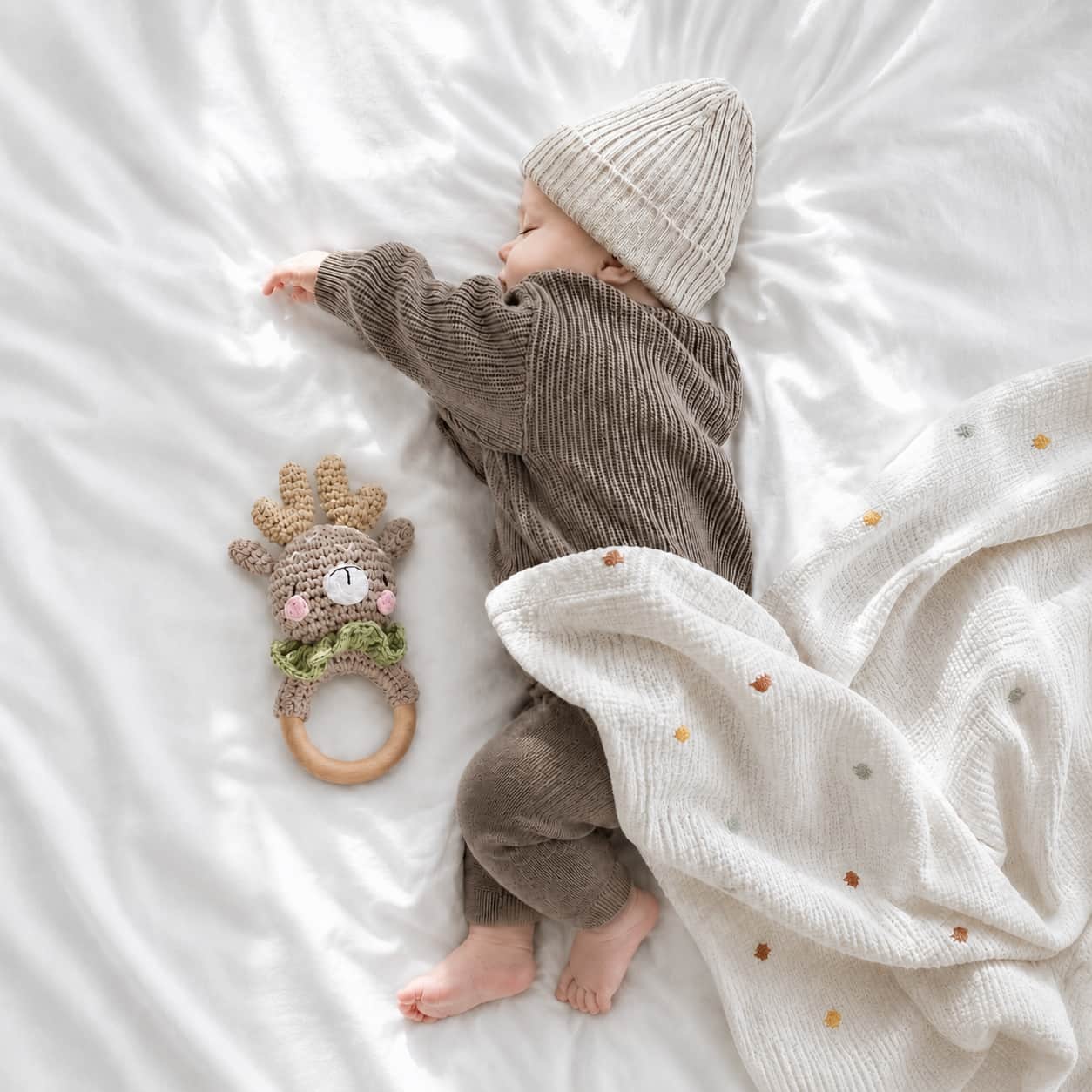 Sleeping newborn baby wrapped in a spotted baby blanket beside a crochet deer teether, a thoughtful baby shower gift and newborn essential in the UK.