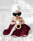 Newborn baby wrapped in a tassel burgundy baby blanket holding a crochet giraffe teether, a thoughtful baby shower gift and newborn essential in the UK.