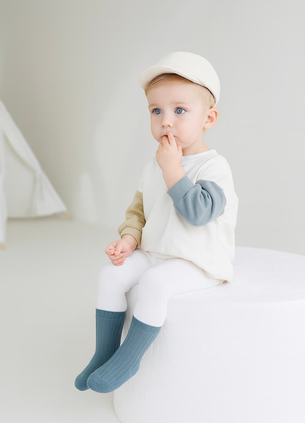Toddler boy sitting in white outfit wearing blue ribbed cotton socks
